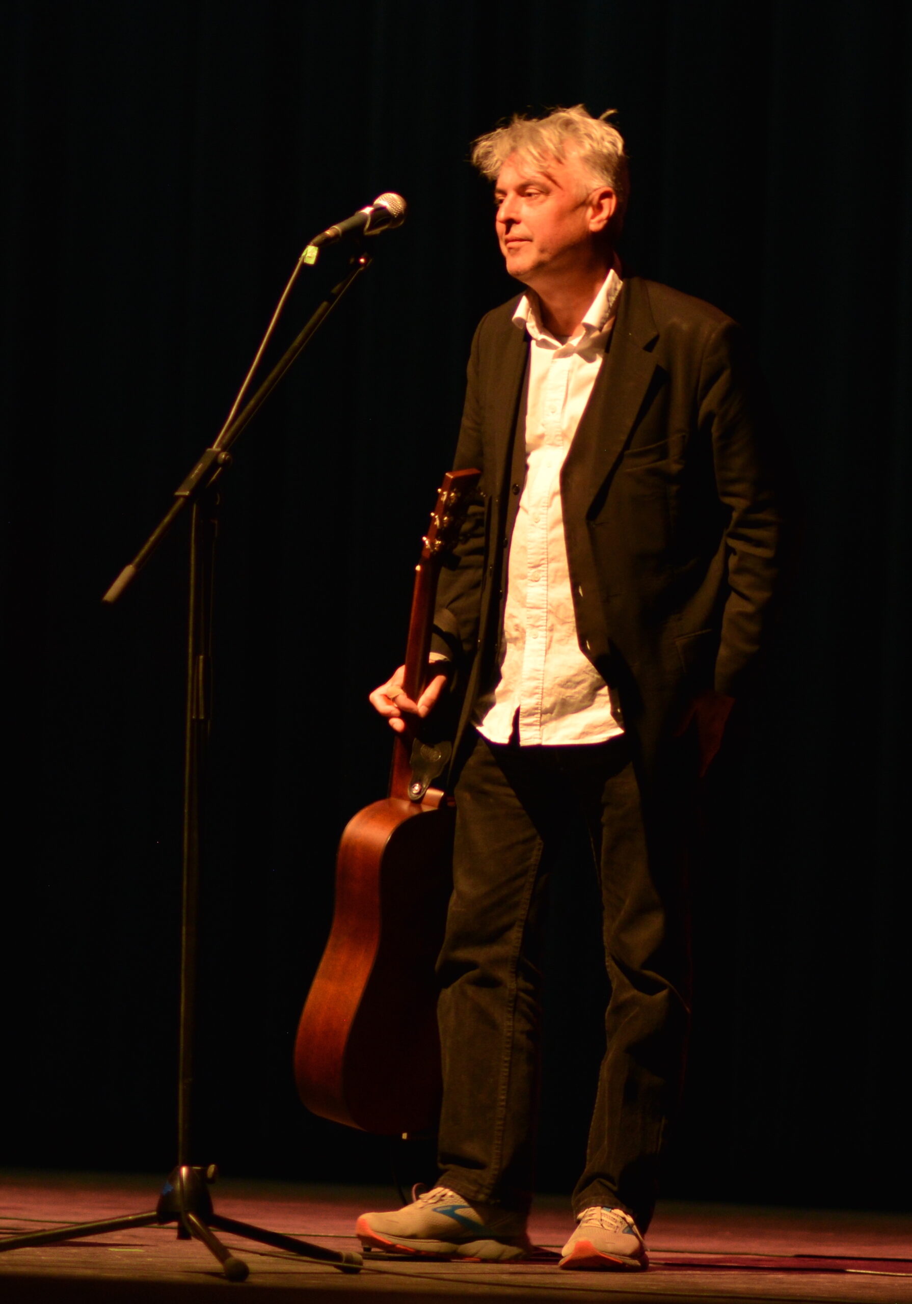 May be a man in a rumpled suit holding a guitar by the next at his side