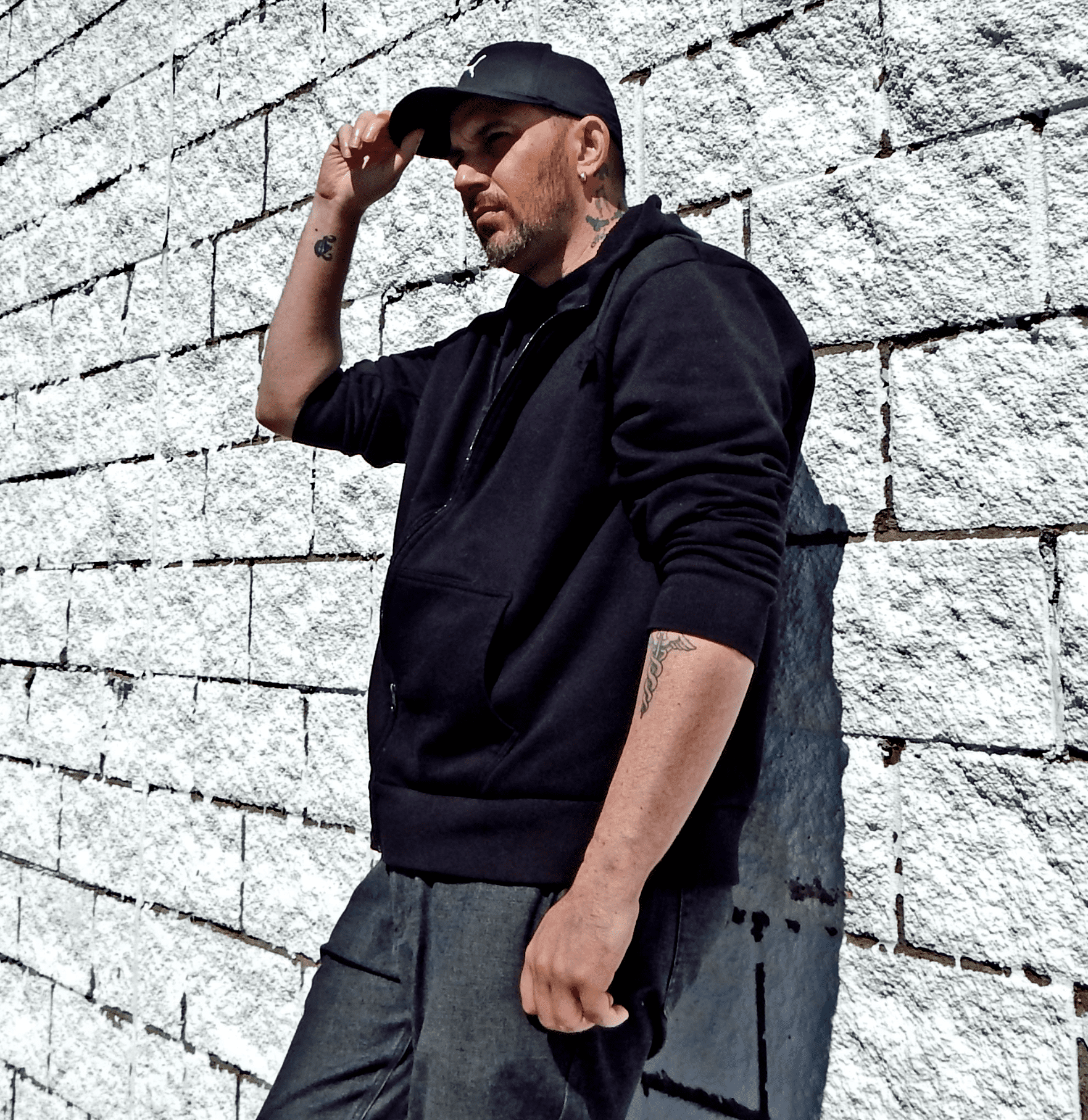 Wild Oscah leaning against a white brick wall looking sexy and stoic.