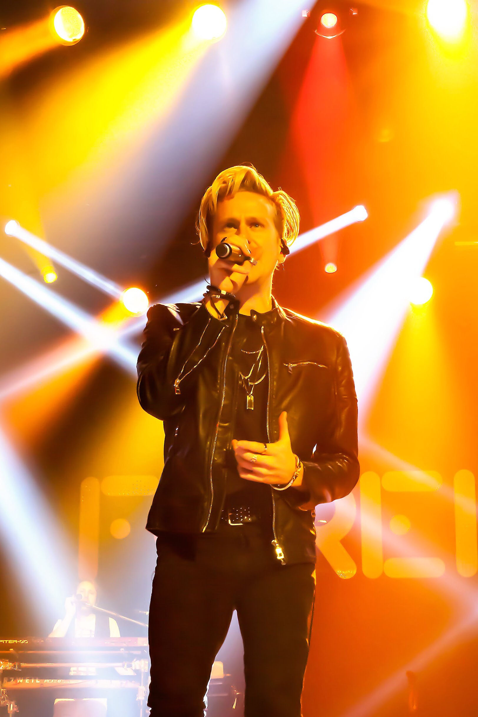 Geordie Brown sings with dramatic stage lights behind him.